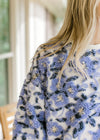 Close up of fuzzy blueish purple flowers on a cream sweater with long sleeves. 