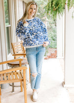 Model wearing jeans with a white sweater with bluish purple elevated flowers and long sleeves. 