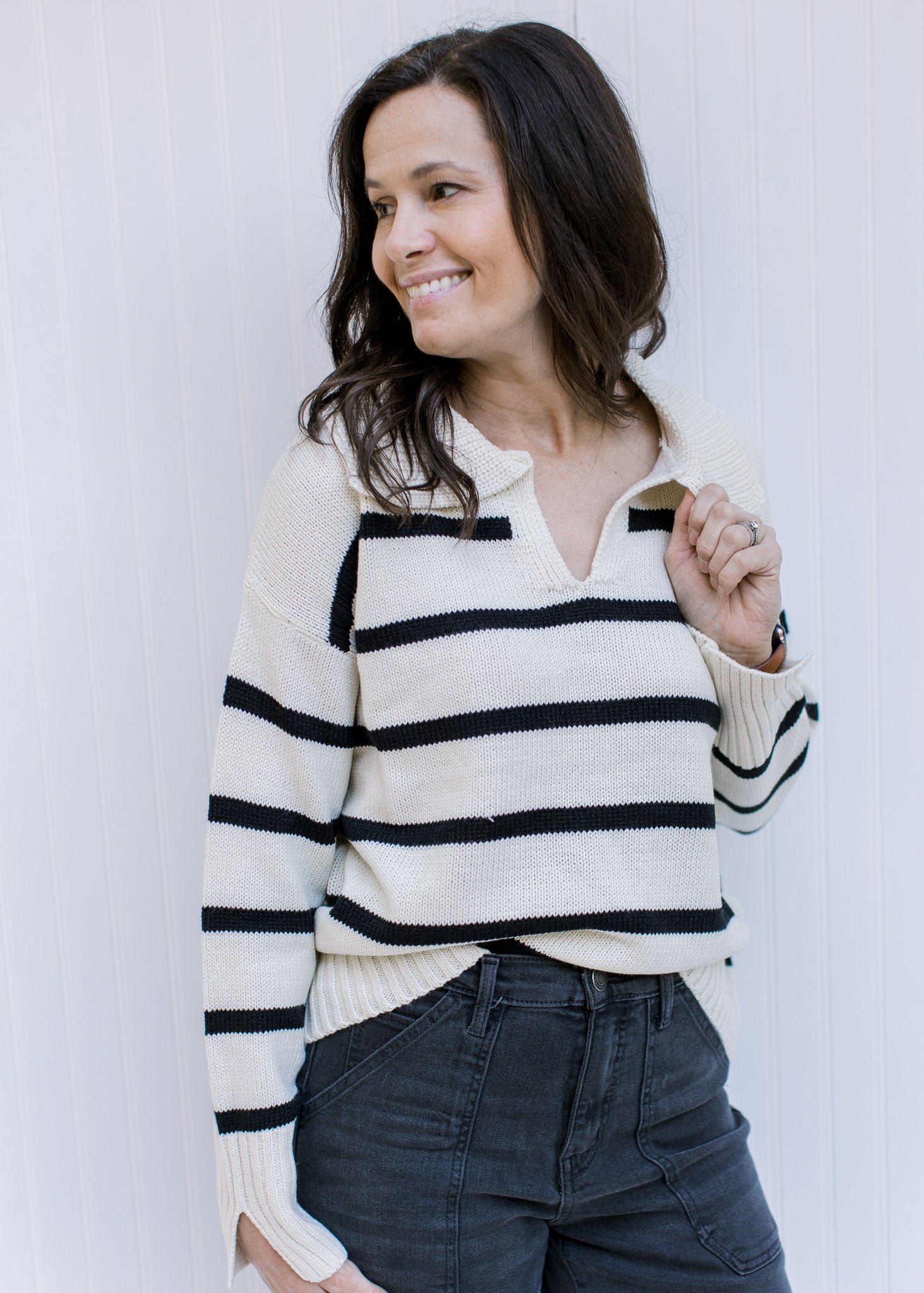 Model wearing a white long sleeve sweater with black stripes, a split hem and a collard v-neck. 
