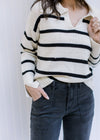 Model wearing black jeans with a white long sleeve sweater with black stripes and a collard v-neck. 