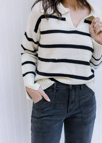 Model wearing black jeans with a white long sleeve sweater with black stripes and a collard v-neck. 