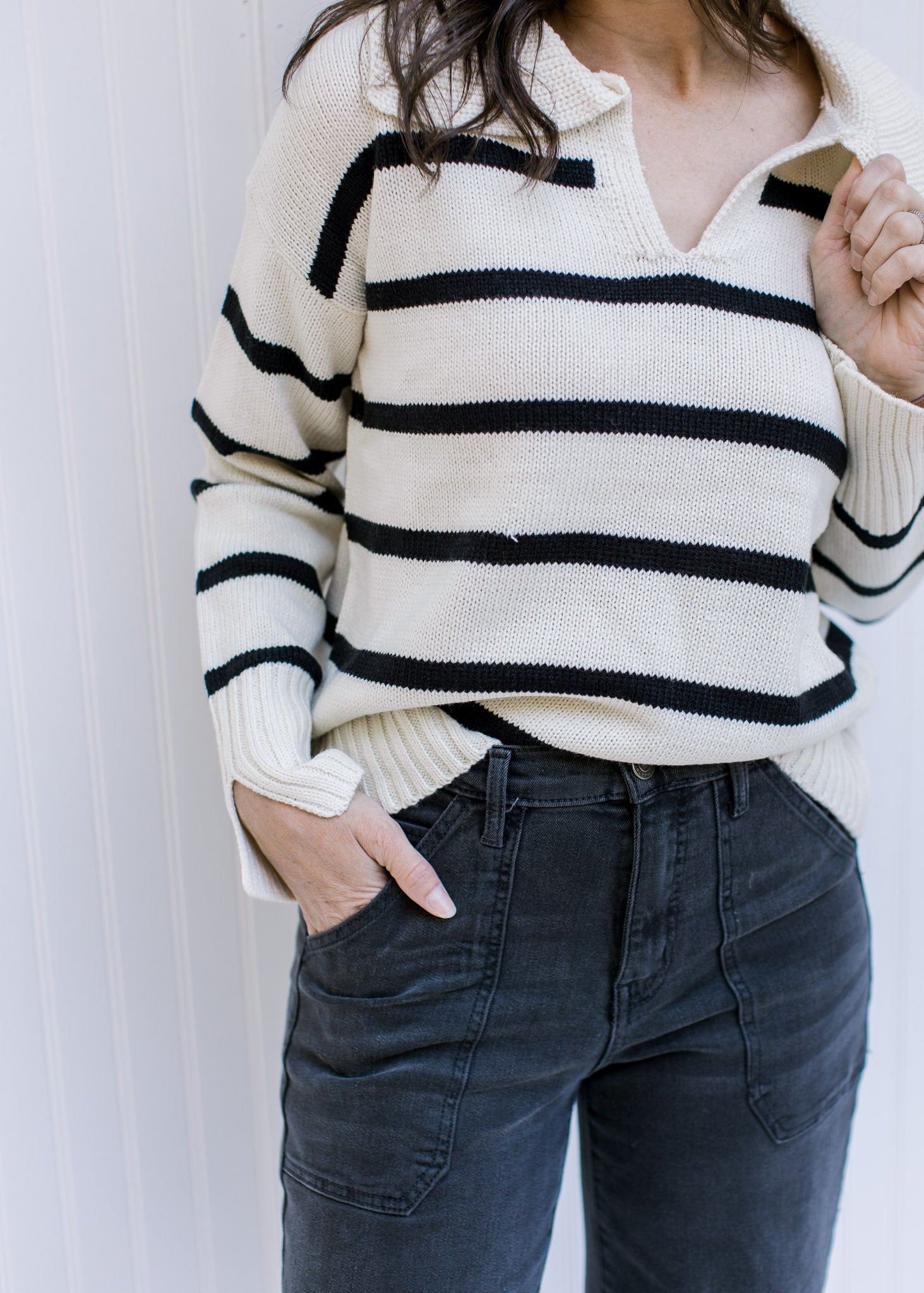 Model wearing black jeans with a white long sleeve sweater with black stripes and a collard v-neck. 