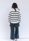 Back view of Model wearing a white long sleeve sweater with black stripes and a split hem. 