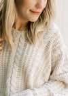 Close up of a model wearing a cream cable knit sweater with a v-neck and long sleeves. 