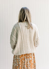 Back view of Model wearing a cream cable knit acrylic sweater with a v-neck and long sleeves.