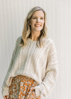 Model wearing a cream cable knit sweater with an acrylic material, v-neck and long sleeves. 