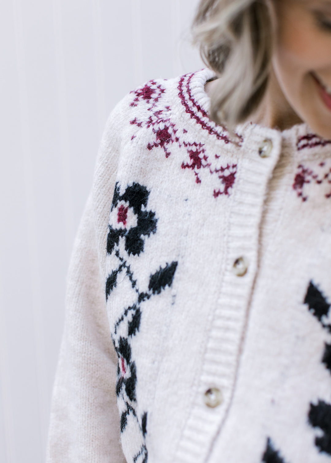 Close up of maroon detailing at the round neck on a cream cardigan with navy floral design. 