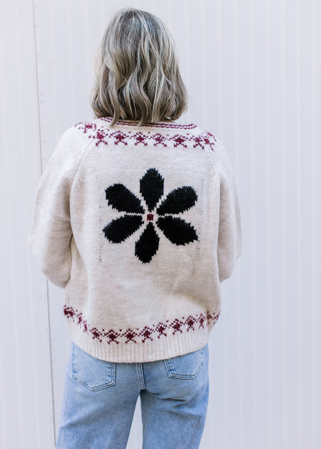Back view of a navy flower and maroon detailing at neck and hem of a cream cardigan. 
