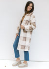 Model wearing a cream, tan and brown plaid knee length coat with pockets and an open front. 
