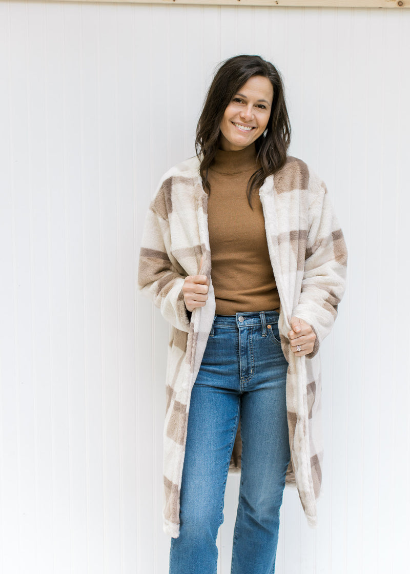 Model wearing a camel top and jeans with a cream, tan and brown plaid coat with an open front. 