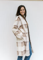 Model wearing a cream, tan and brown plaid coat with an open front, pockets and long sleeves. 