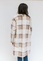 Back view of Model wearing a camel top with a cream, tan and brown plaid, knee length coat. 