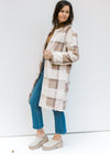 Model wearing jeans and mules with a cream, tan and brown plaid knee length coat with an open front.