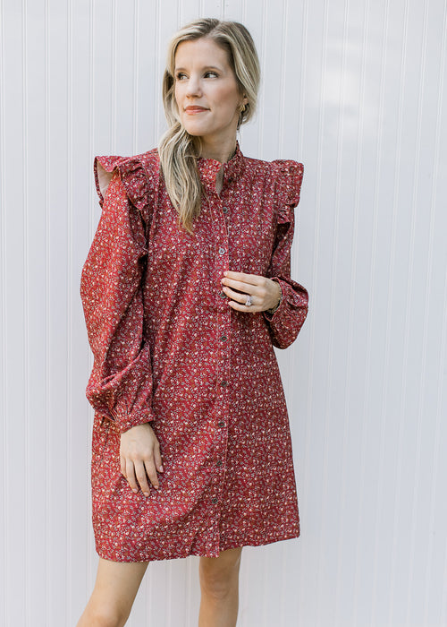 Model wearing a rust dress with cream ditsy floral, button front and ruffle at the shoulder. 