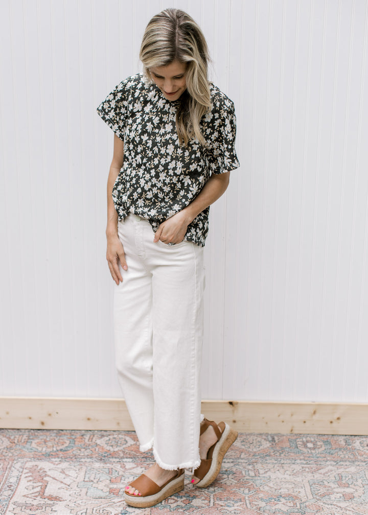 Model wearing white jeans and a black top with white daisies and short sleeves.