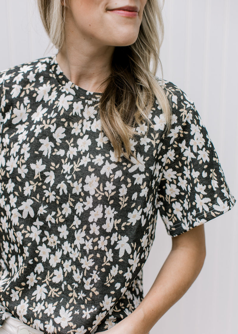 Close up view of white daisies on a black top with a round neck and short sleeves. 