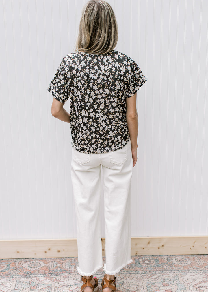 Back view of Model wearing a black top with white daisies and short sleeves.