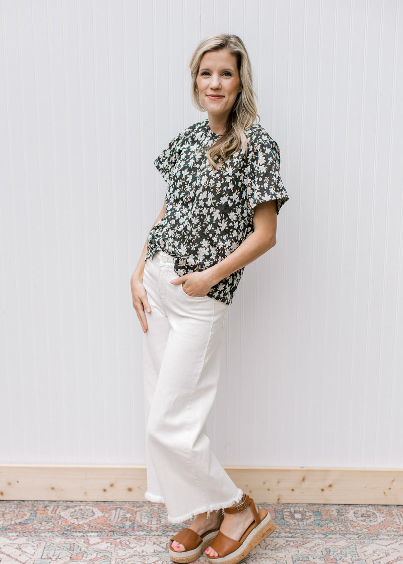 Model wearing white jeans with a black top with white daisies, a round neck and short sleeves. 