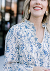 Close up of pleating on the bodice and ruffle neck with tie on a cream top with blue floral. 