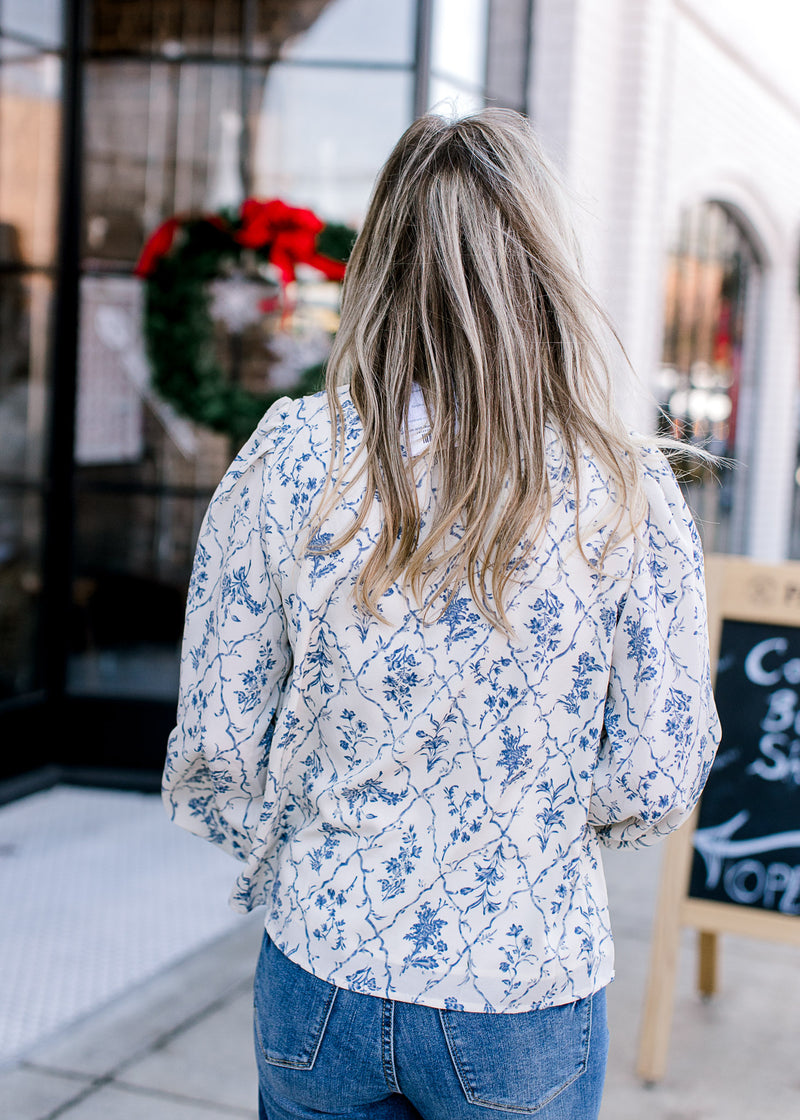 Back view of Model wearing a cream top with blue floral print, long bubble sleeve with elastic cuff.