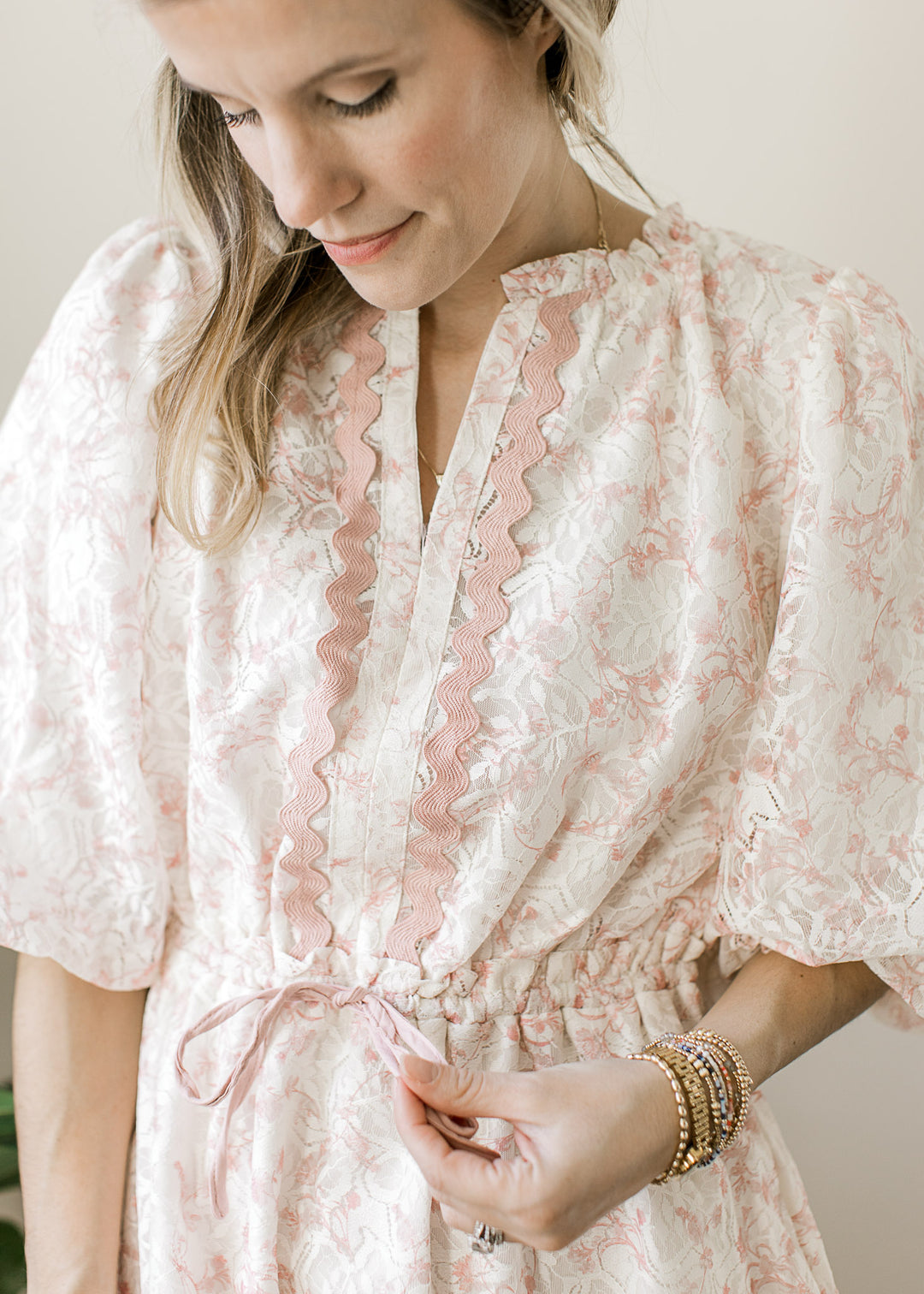 Close up of blush scalloped trim, v-neck and tie waist on a cream above the knee dress with floral.