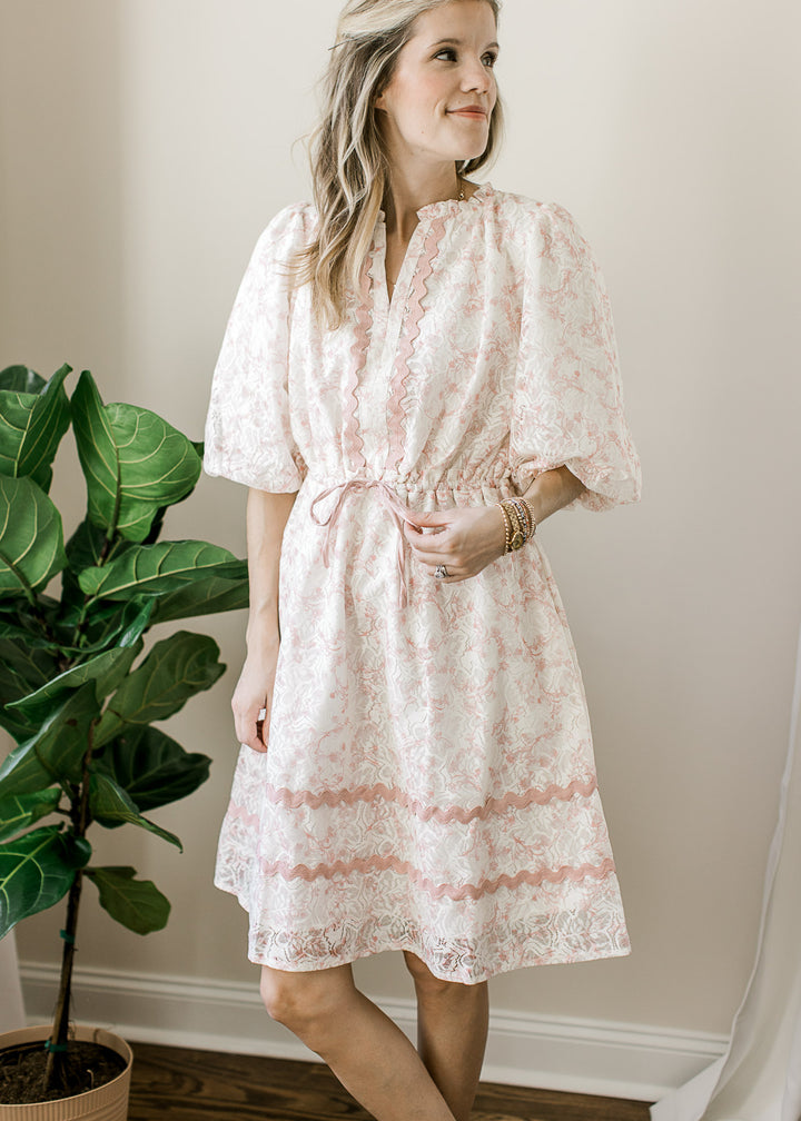 Model wearing a cream dress with blush floral and scallop trim, 3/4 sleeves and tie waist. 