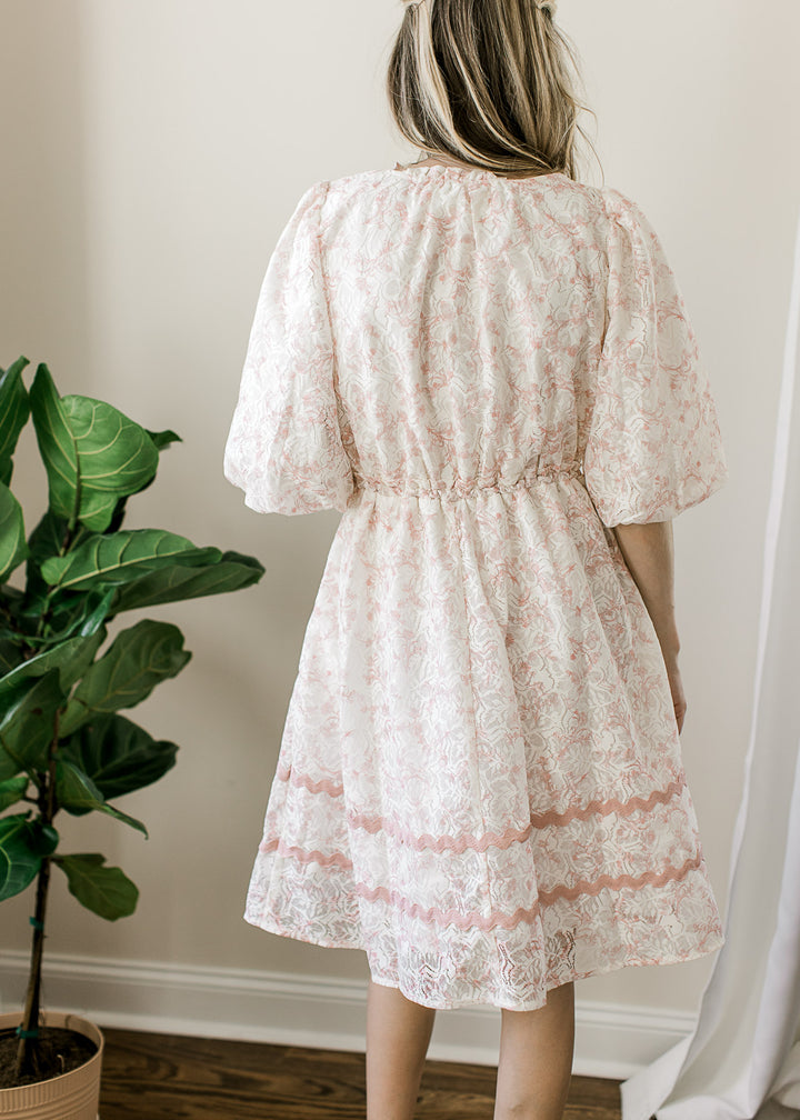 Back view of model wearing a cream dress with blush floral, blush scalloping detail and 3/4 sleeves.