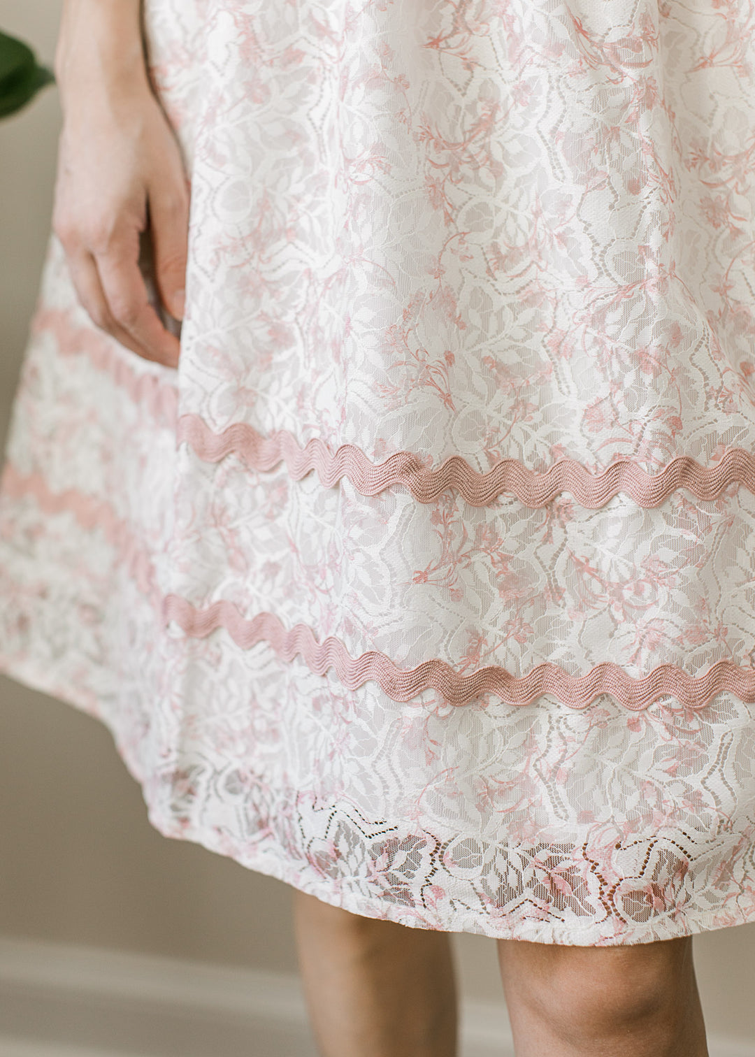 Close up of scalloped trim on a cream above the knee dress with lace overlay. 