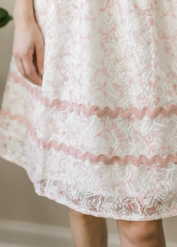 Close up of scalloped trim on a cream above the knee dress with lace overlay. 