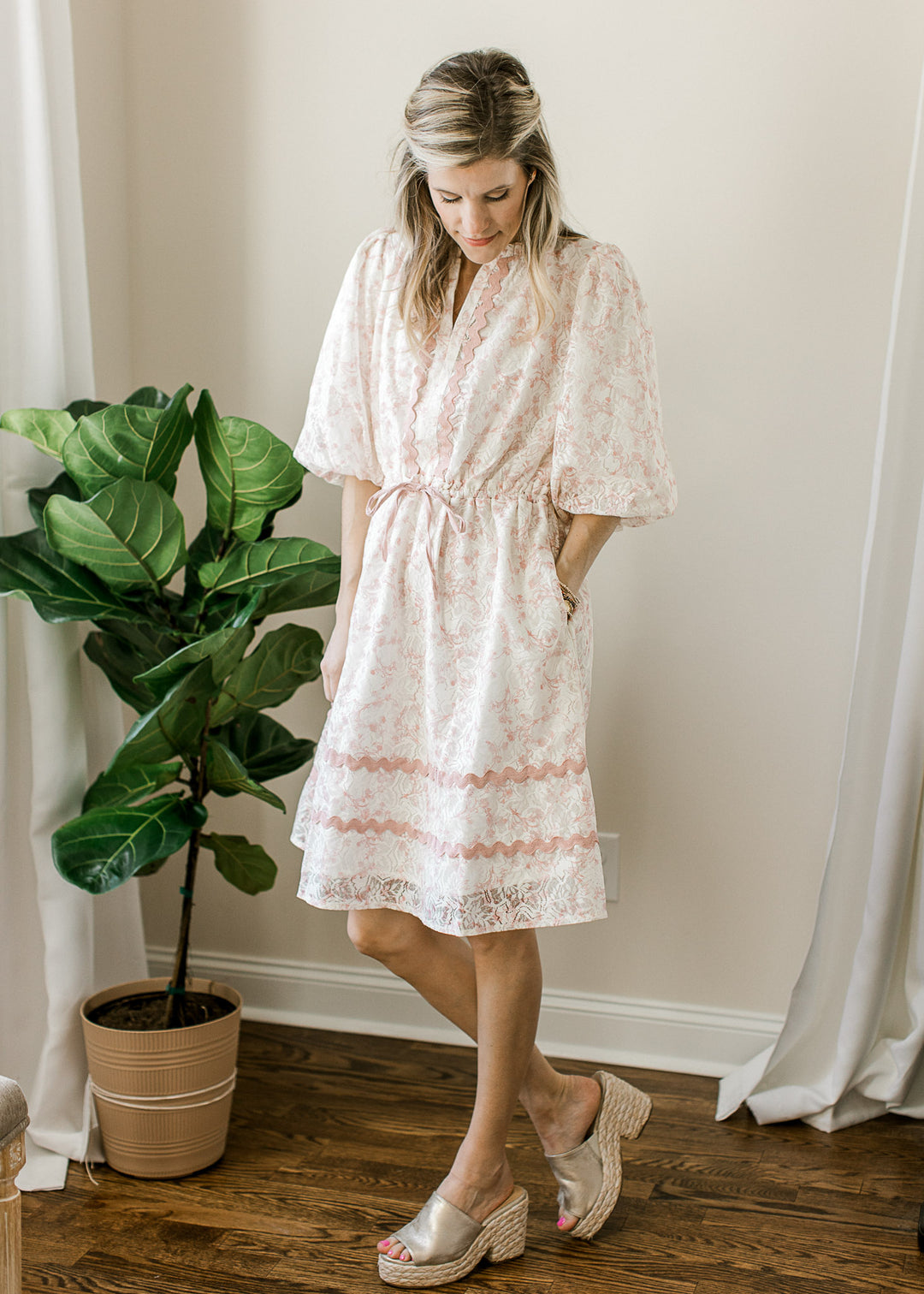 Model wearing wedges and a cream dress with lace overlay with blush floral and 3/4 bubble sleeves.