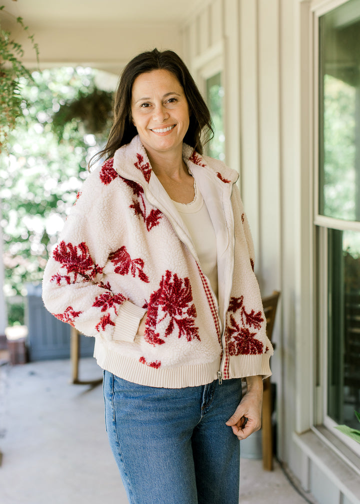 Model wearing jeans and a plush jacket with cream with burgundy floral and long sleeves. 
