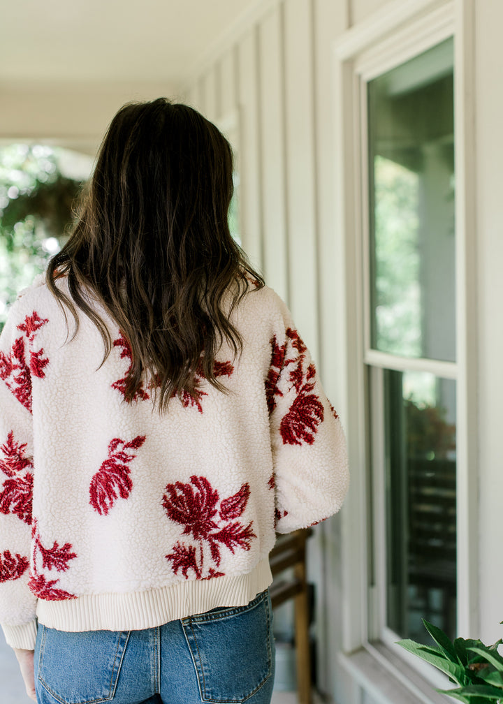 Back view of Model wearing a cream jacket with burgundy floral, mock neck and long sleeves. 