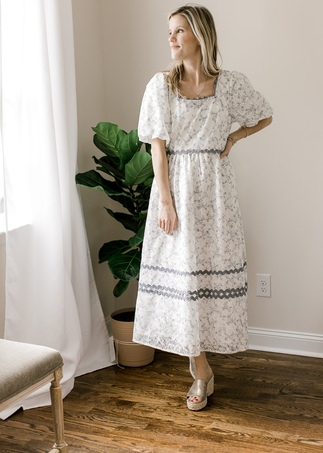 Model wearing a cream midi with dusty blue floral, lace overlay, scallop detail and square neckline.