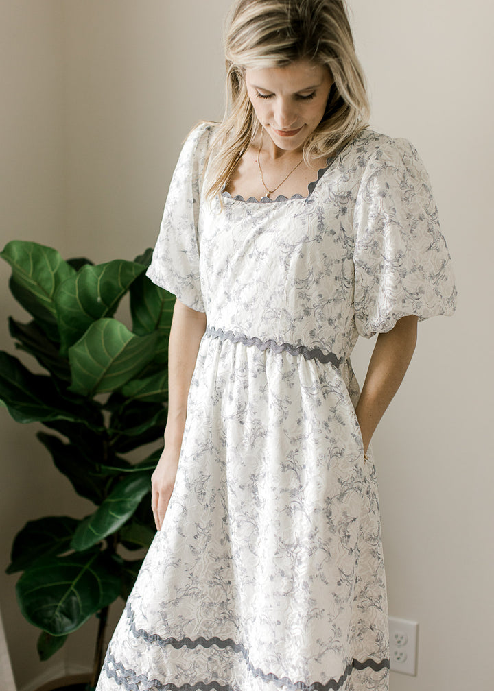Model wearing a cream dress with dusty blue floral, bubble short sleeves and square neckline. 