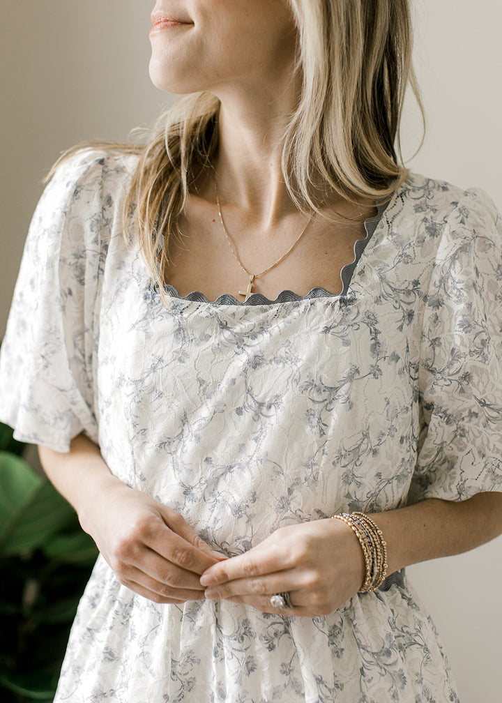 Close up of square neck with dusty blue scalloping on a cream midi with floral and short sleeves.