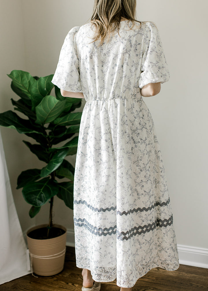 Back view of Model wearing a cream midi with dusty blue floral, elastic waist and short sleeves.