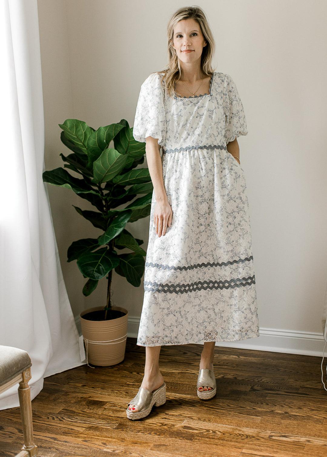 Model wearing a cream midi with dusty blue floral and scalloping, square neck and short sleeves.