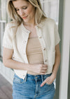 Model wearing jeans, cami and a cream short sleeve sweater with gold buttons and patch pockets. 