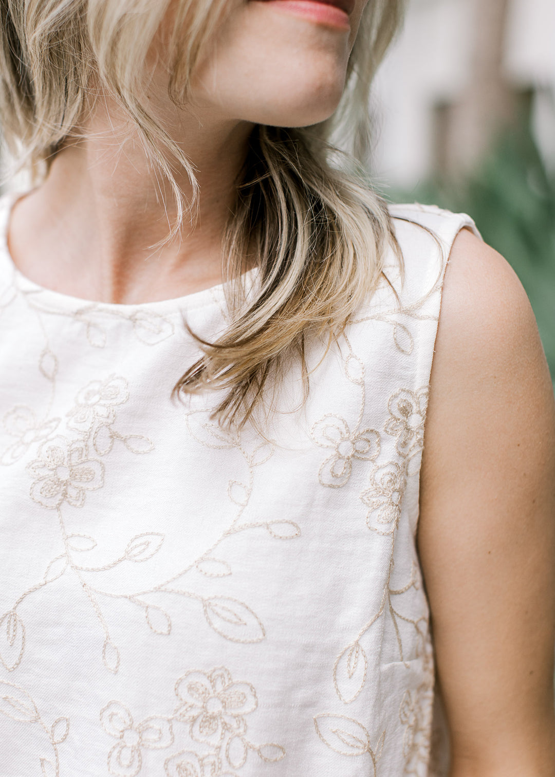 Close up of tan embroidered floral on an ivory top with round neck and slightly cropped fit.