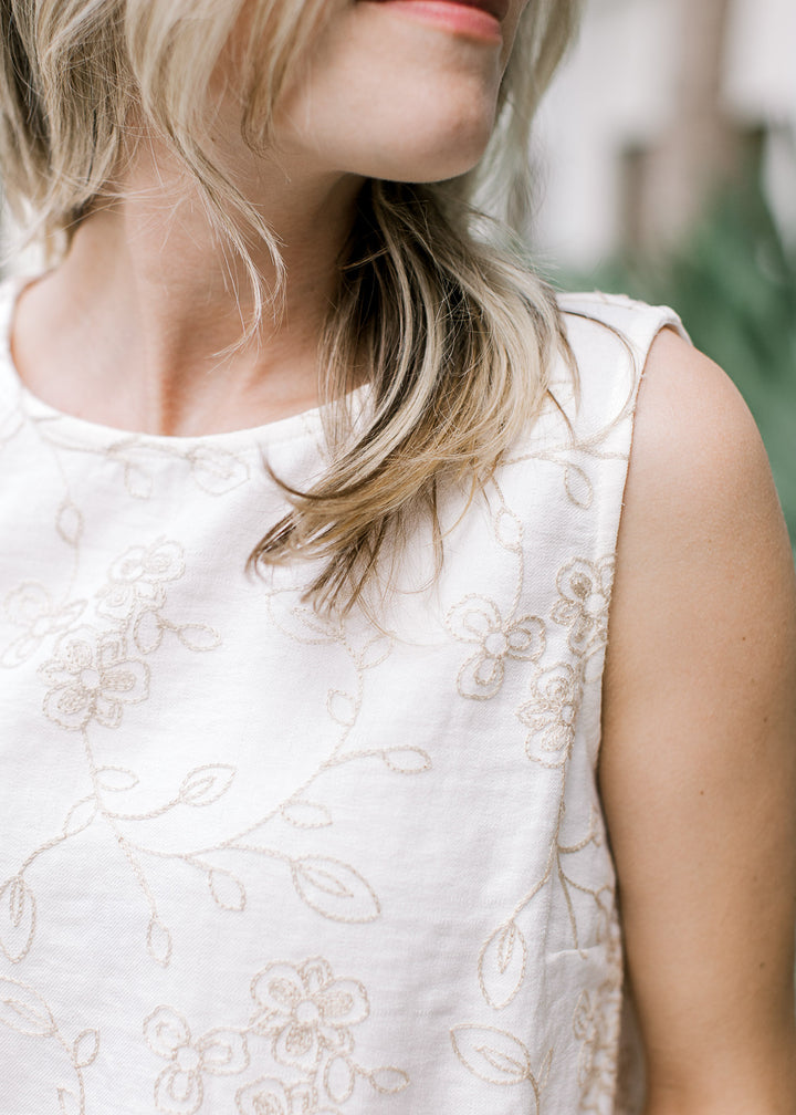 Close up of tan embroidered floral on an ivory top with round neck and slightly cropped fit.