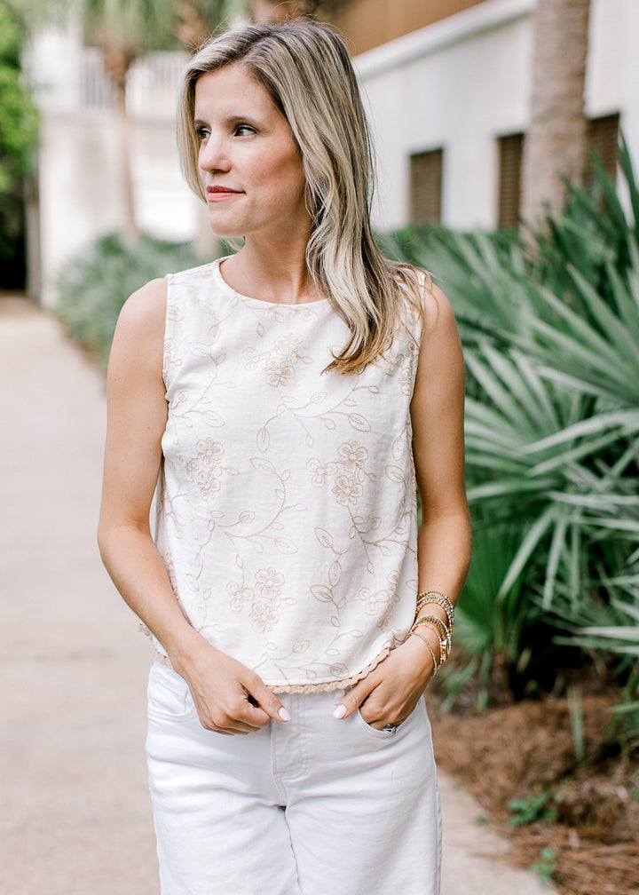 Model wearing white pant and an ivory sleeveless top with tan floral and tan scalloped trim.