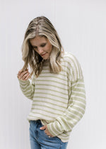 Model wearing a cream and lime striped sweater with inverted pattern on the long sleeves. 