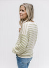 Side view of Model wearing a cream and lime striped sweater with inverted pattern on the sleeves. 