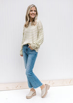Model wearing jeans, mules and a cream and lime striped sweater with inverted pattern on  sleeve.