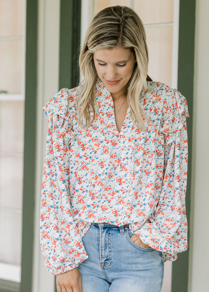 Model wearing a cream top with orange and blue floral, long sleeves, v-neck and a flowy fit. 