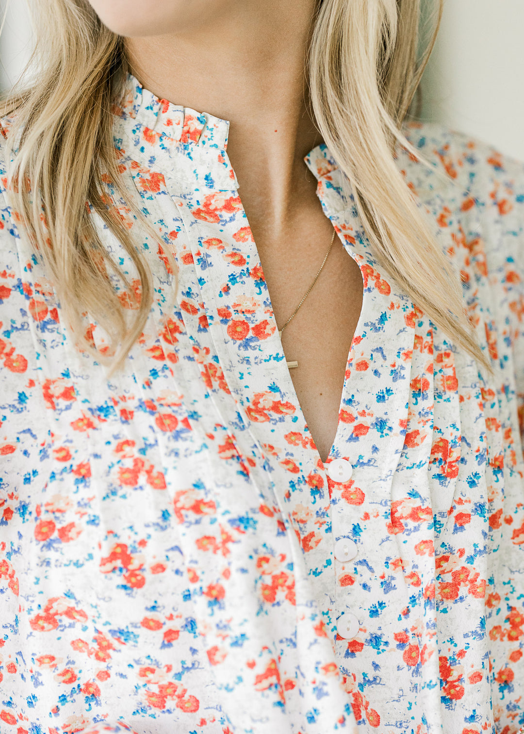 Close up of v-neck with ruffle and pleating on a cream top with orange and blue floral pattern. 