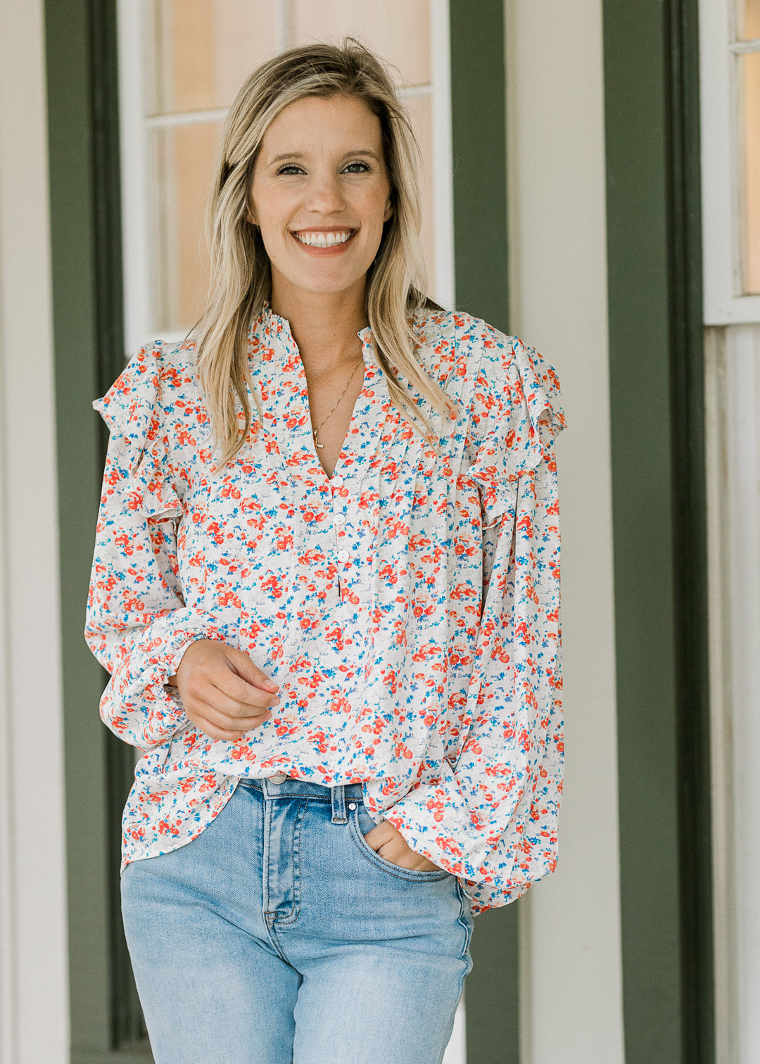 Model wearing jeans and a cream blouse with orange and blue floral, long sleeves and a v-neck.