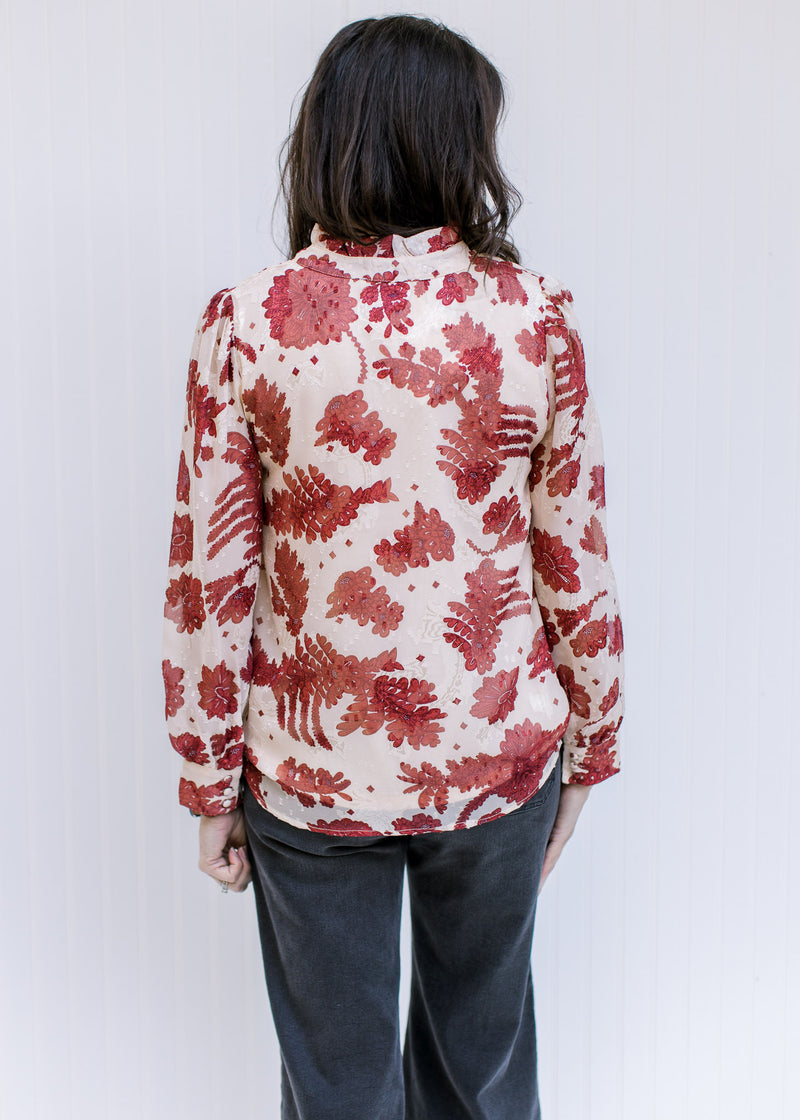 Back view of a model wearing a cream polyester top with rust floral and sheer long sleeves. 