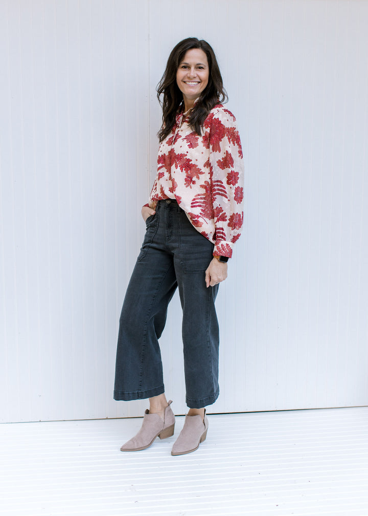 Model wearing a cream polyester top with rust floral, sheer long sleeves and a v-neck with a tie. 