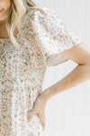 Close up of elastic on square neckline and flutter short sleeves on a cream dress with pink floral.